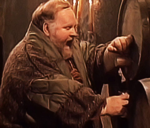 A screencap of Ritch as William, pulling a beer from the barrel at Winterfest, a big smile on his face.