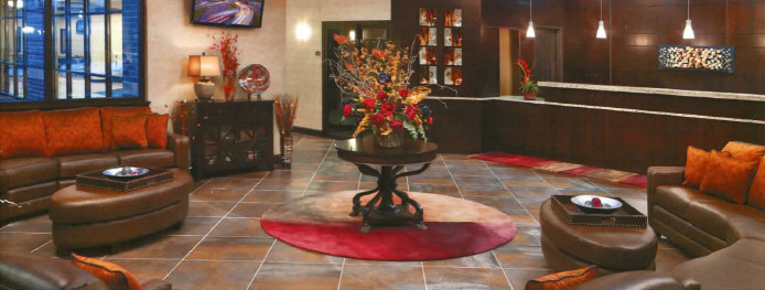 Entering the lobby from the front door, there are windows on the left and right sides of the room. The front desk is directly in front of you. There are 2 curved leather couches, one on each side of the room, with a large oval footstool in front of each. There's a decorative table in the center with a vase of dried flowers. The restaurant is to the right of the check-in desk. To the left of the check-in desk is a hallway which leads to (off screen: shared computers, the breakfast room, the meeting room, and all guest rooms).