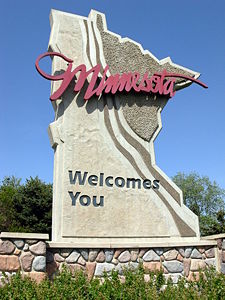 road sign at Minnesota border, in the shape of Minnesota; text Minnesota welcomes you