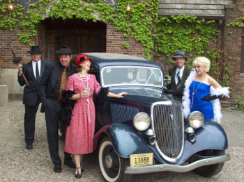 an old car, surrounded by people dressed as gangsters