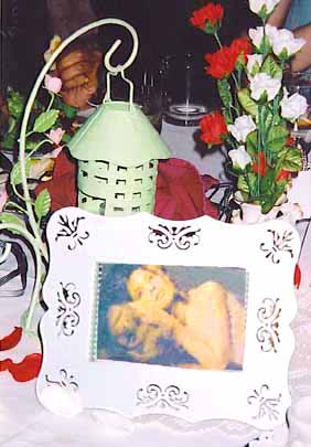 banquet centerpiece: pale green candle lantern suspended on a wire hook, red and white roses (artificial) in a vase; a framed photo of the publicity photo where Cathterine's head is on top of Vincent's