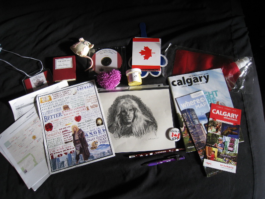 from top left, going clockwise, name badge, mini book of Shakespeare's sonnets, cat toy, conzine on disc, heart-shaped plushie screen cleaner, Canada notebook, paw shaped fan, hand-made body butter, flat water bottle, Calgary tourism magazine and flyers, Canada button, Canada pencil, Port Pirie RDA pen, original Lynn Wright sketch, print of Sandy Tew quote poster, maps of local area, con schedule